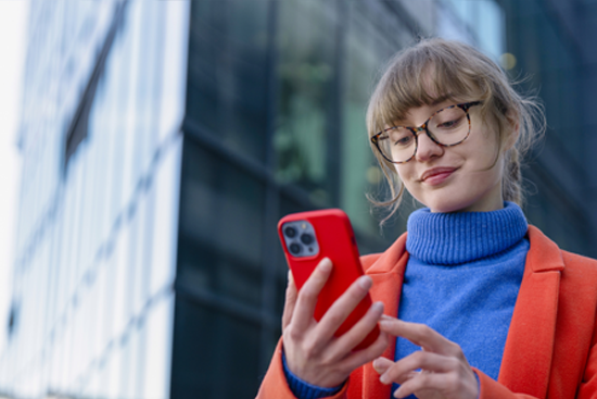 Young woman in orange jacket using smartphone in the street.